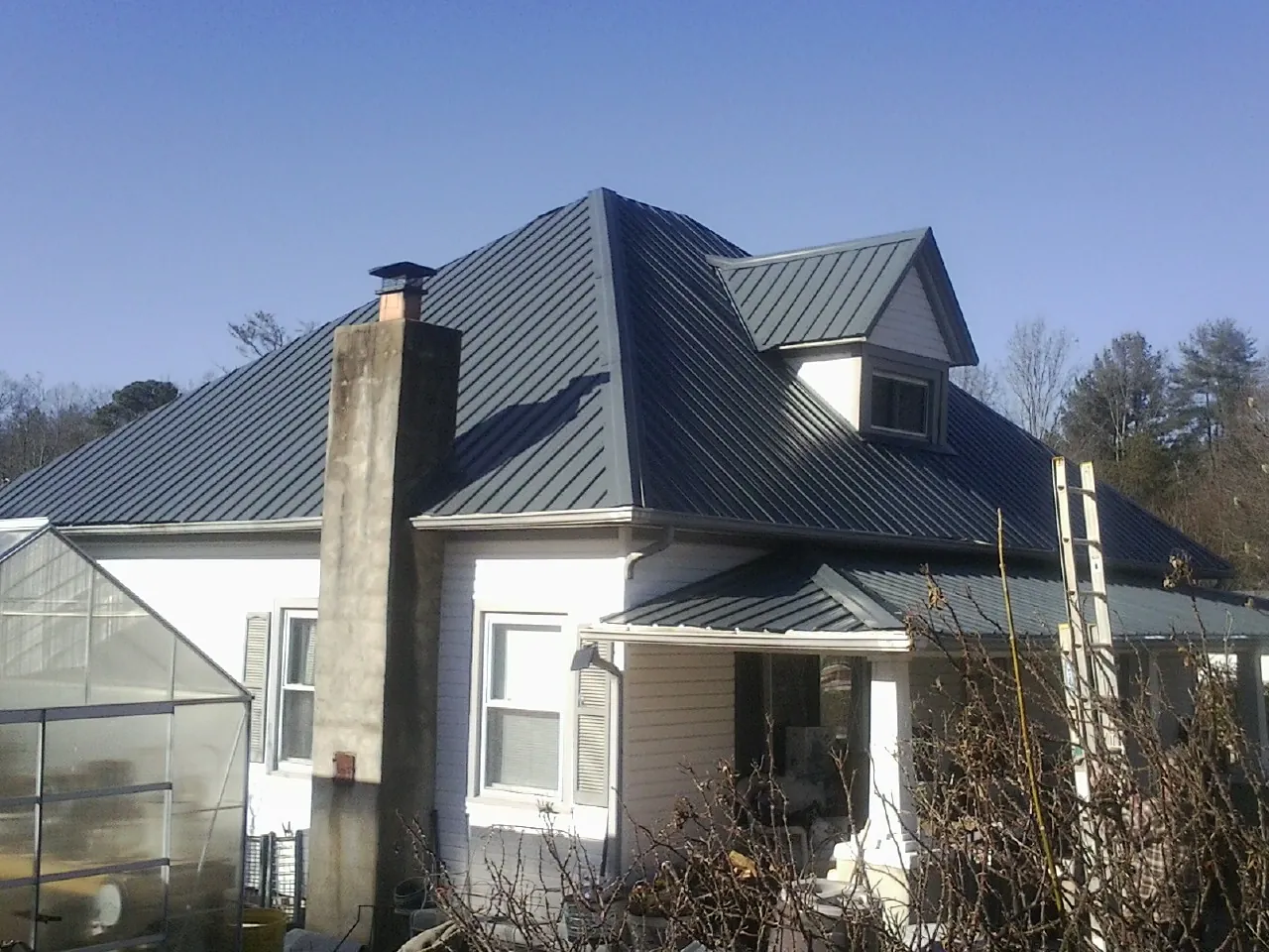 Dark blue standing seam metal roof on a white farmhouse with dormer — Slate & Tile Roof Repair by Roofing Brothers in Pell Lake
