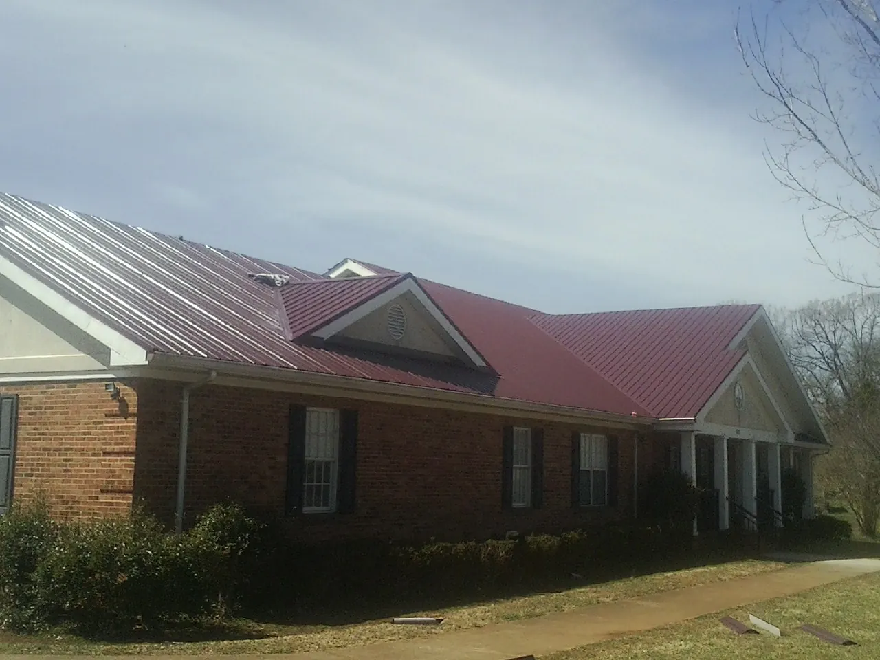 Red metal roof with gabled entries on a long brick building, from a Hail Damage Roof Repair job in Pell Lake