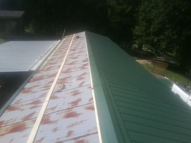 Old rusted panels beside newly installed green metal roofing — Wind Damage Roof Repair by Roofing Brothers in Pell Lake