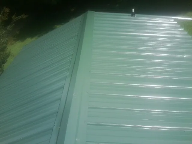 New green metal panels meeting at the ridge of a roof — Flat Roof Repair work by our crew in Pell Lake