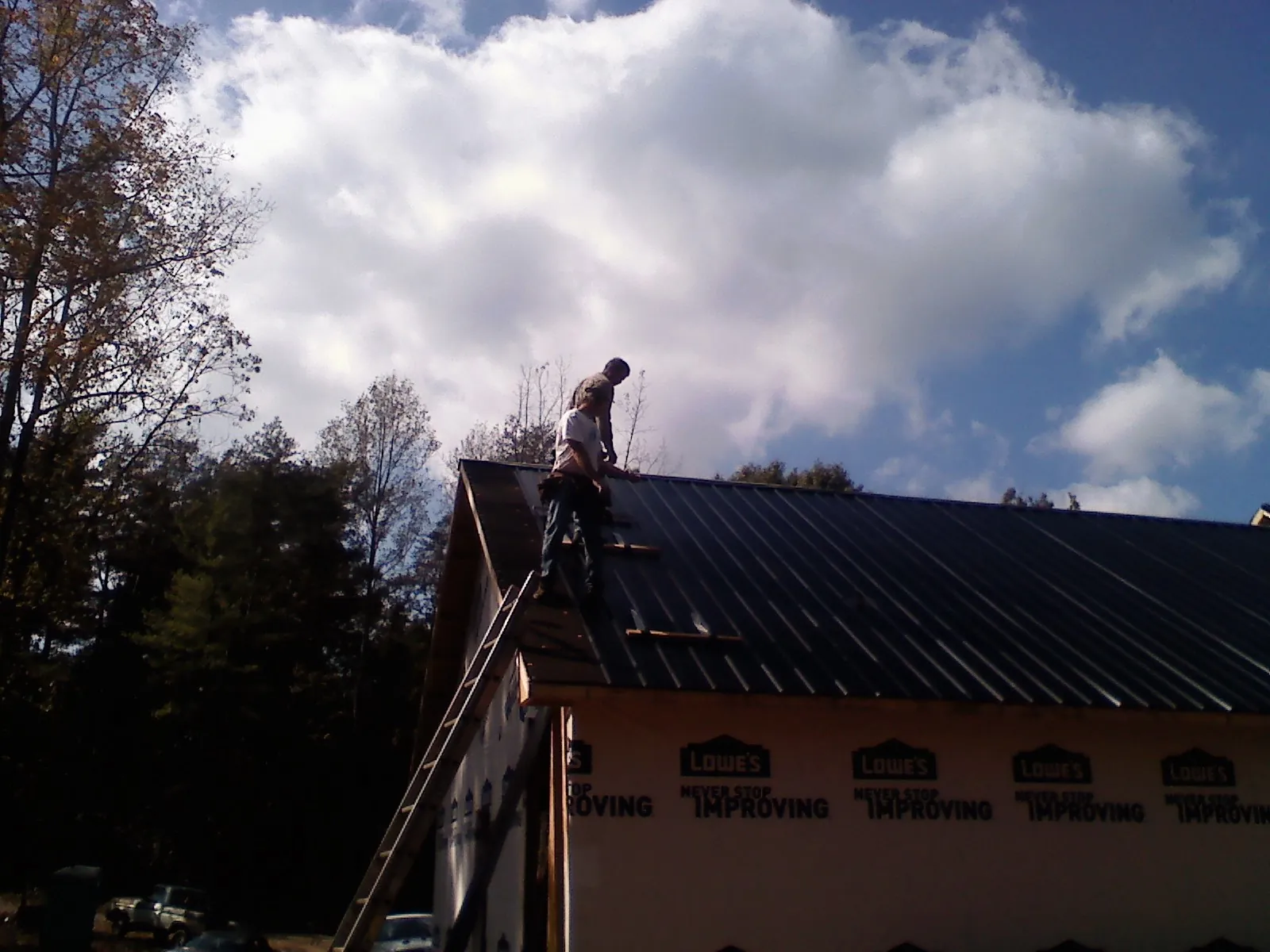 Roofer fastening dark metal panels high against a cloudy sky, from a Roof Inspection job in Pell Lake