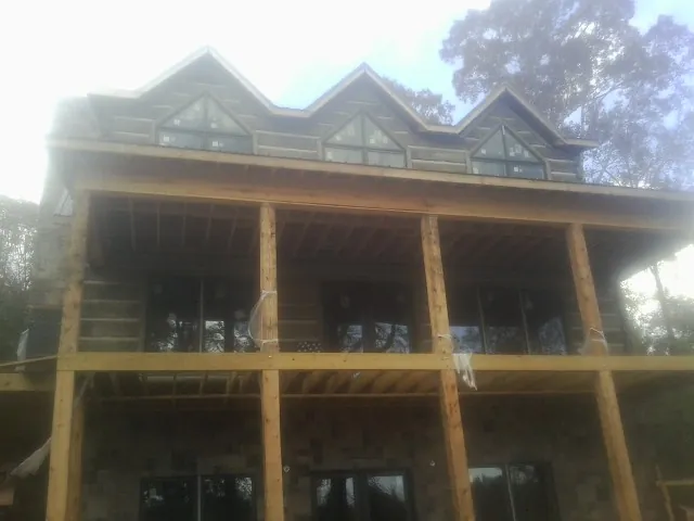 Dormers and porch framing on a large log home under construction — Roof Coating work by our crew in Pell Lake