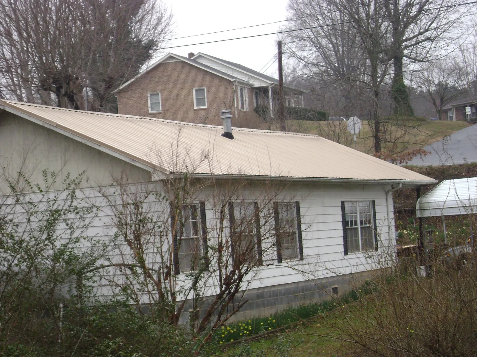 Tan metal roof on a white sided house set into a hillside — Commercial Roofing by Roofing Brothers in Pell Lake