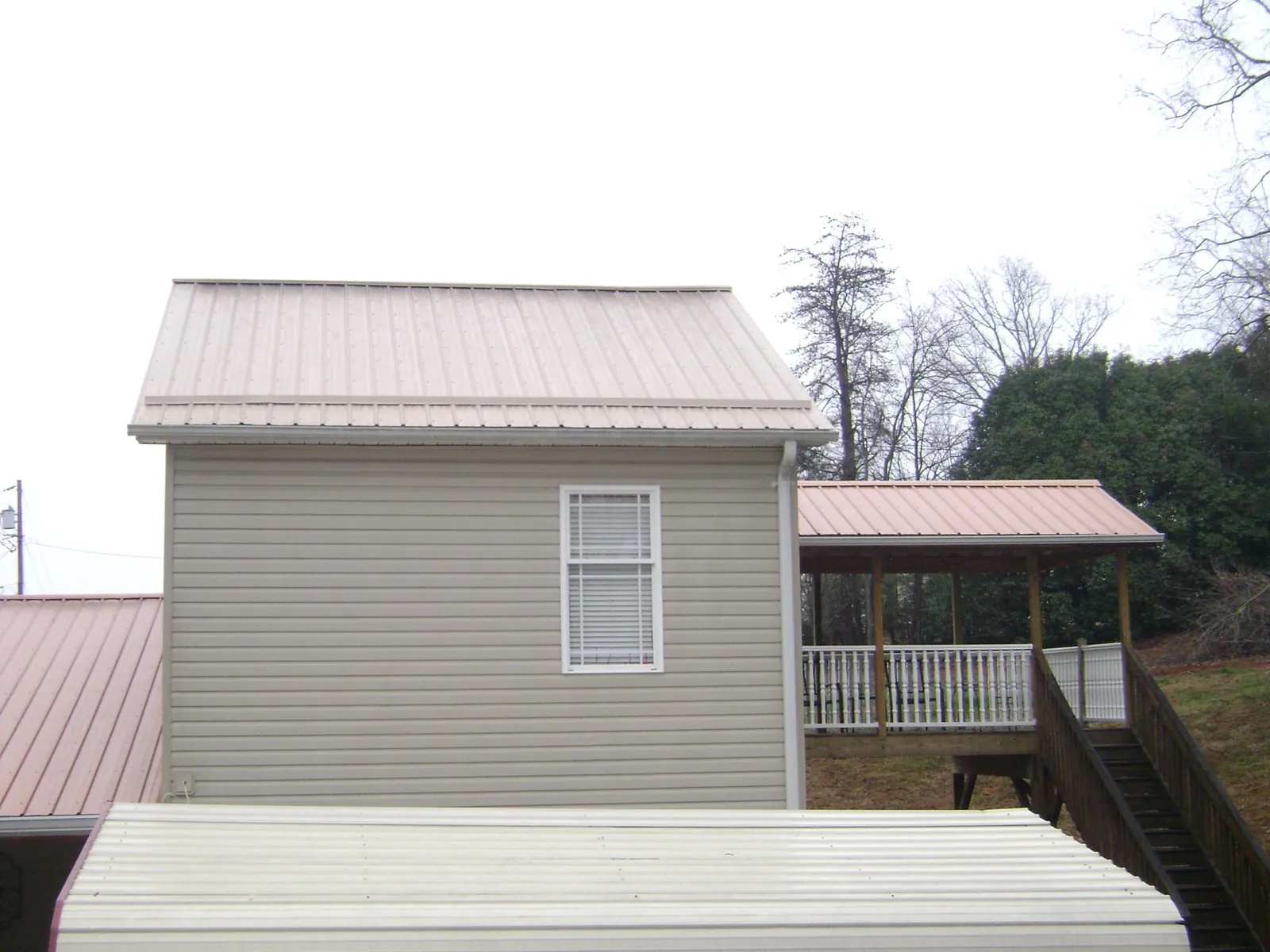 Tan metal roofs on a two story addition and attached porch, from a Roof Replacement job in Pell Lake